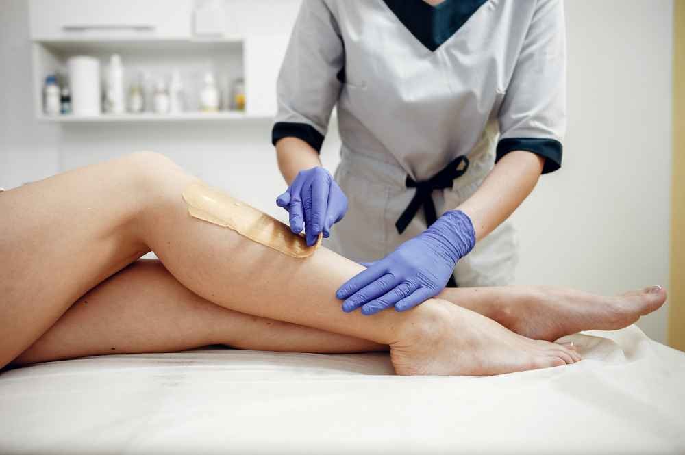 An Image Showing A Hand Applying Sugaring Paste To The Skin, With Ingredients Like Sugar, Lemon, And Water Is At The Side Of The Table