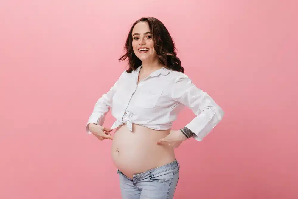 Smiling pregnant woman with smooth skin sitting comfortably post-wax in a salon robe.